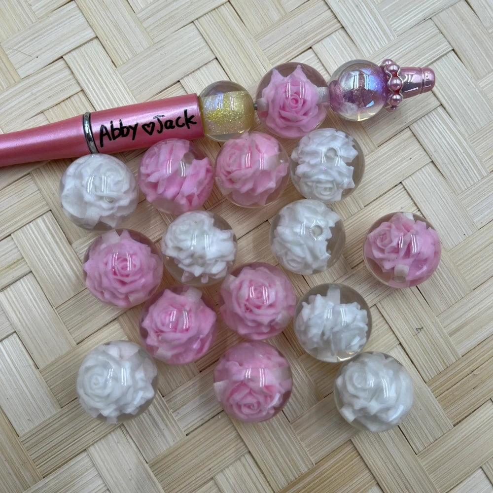 20MM pink and white rose flower acrylic beads displayed on woven mat next to a beadable pen, showing clear sphere beads with embedded floral designs.