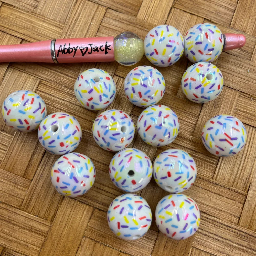 20MM white acrylic round beads with colorful rainbow sprinkle confetti pattern, shown next to a beadable pen on a wicker surface