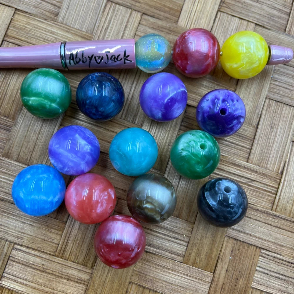 20MM marble swirl acrylic beads in assorted colors including green, blue, purple, teal, red, yellow, pink, and black displayed on a woven surface next to a beadable pen.