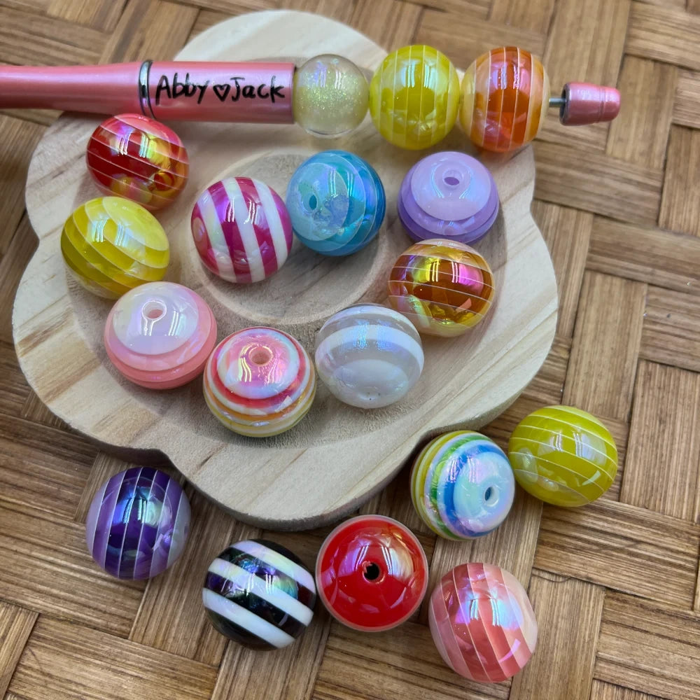 20MM striped rainbow swirl acrylic beads in assorted multicolor patterns including pink, yellow, purple, red, blue, and white stripes displayed on a wooden tray with a beadable pen.