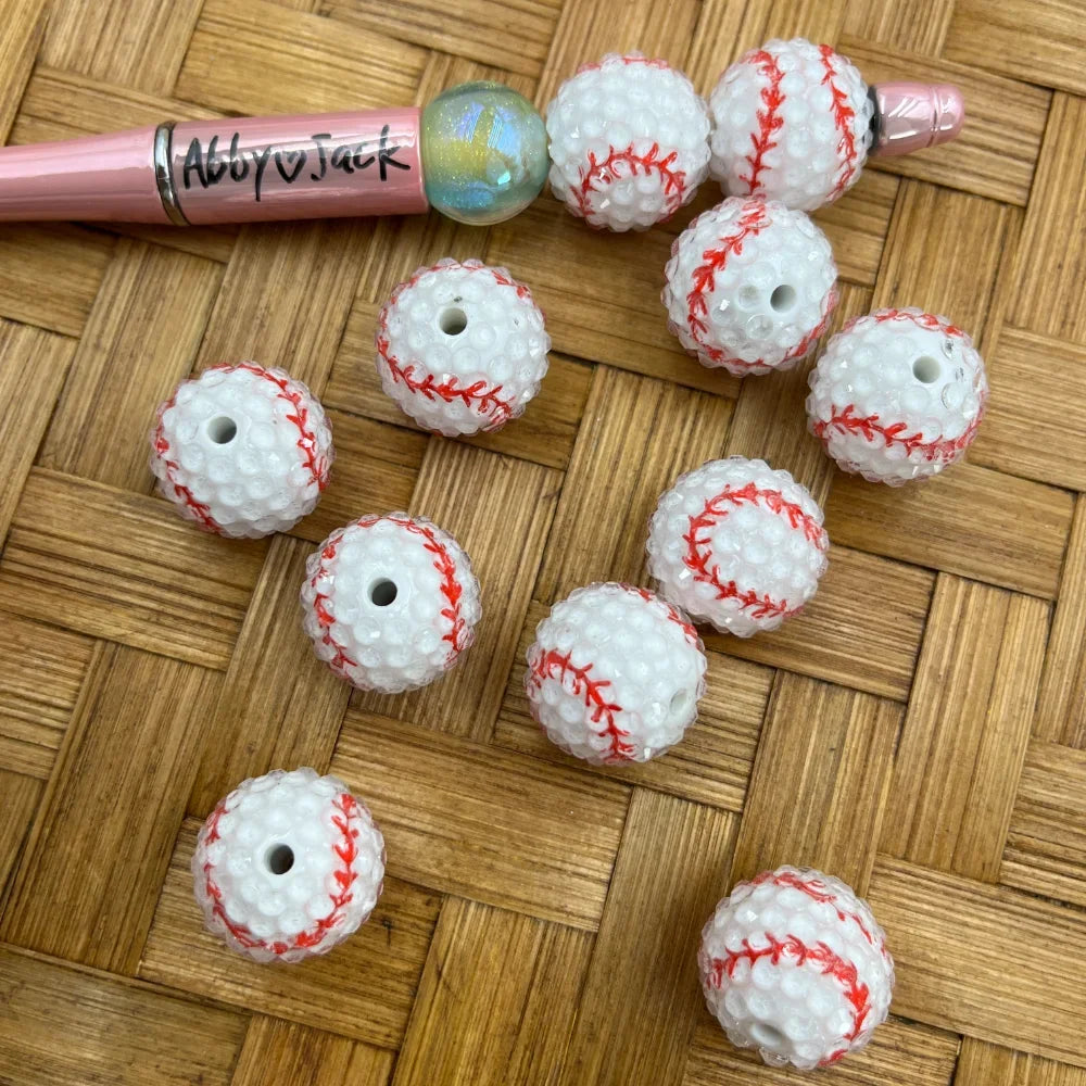 20MM white baseball bumpy acrylic beads with red stitching detail displayed on wicker surface next to a pink beadable pen, showing hole for stringing.