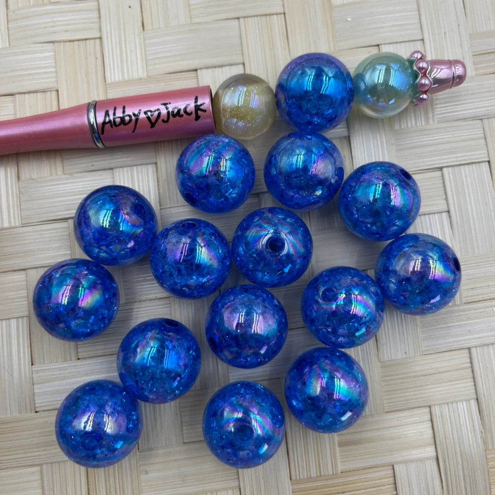 20MM blue iridescent crackle acrylic beads with aurora shimmer finish displayed on woven bamboo surface next to a beadable pen