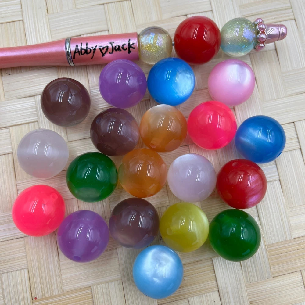 20MM cat eye acrylic beads in assorted colors including red, blue, green, purple, pink, orange, and white on a woven mat next to a beadable pen.