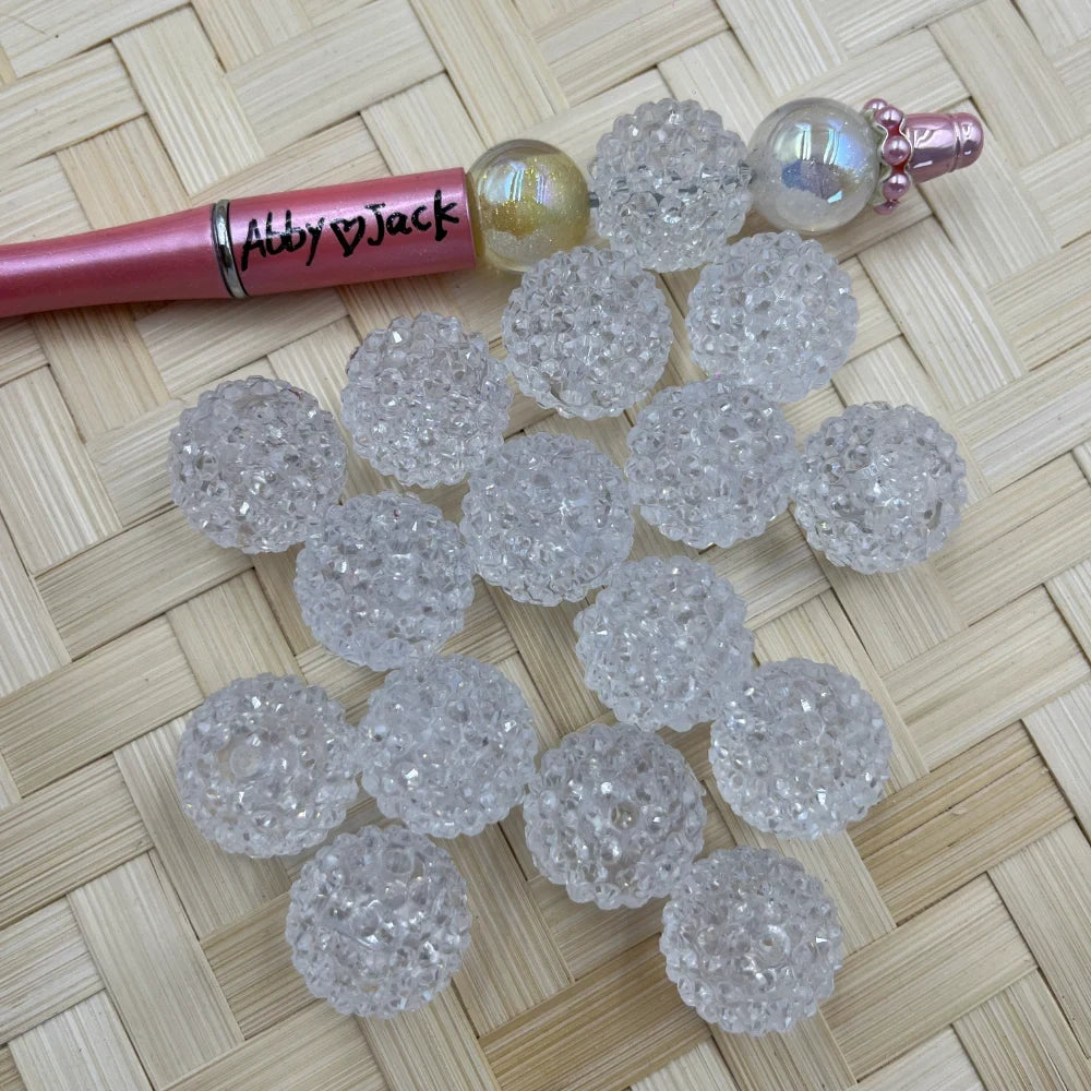 20MM clear crystal rhinestone textured acrylic beads scattered on woven surface next to a beadable pen, showing sparkly bumpy ball bead detail.