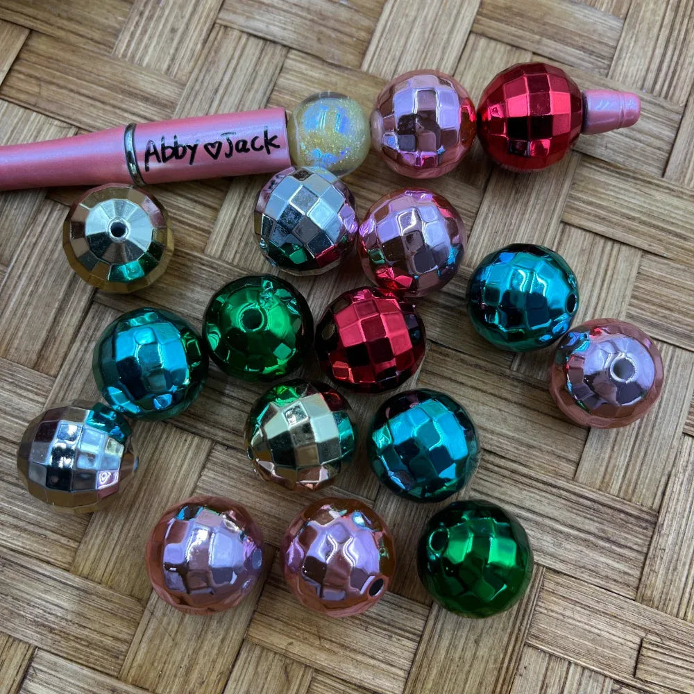 20MM disco ball metallic acrylic beads in red, green, pink, teal, and silver mirror faceted finish displayed next to a beadable pen on a woven surface