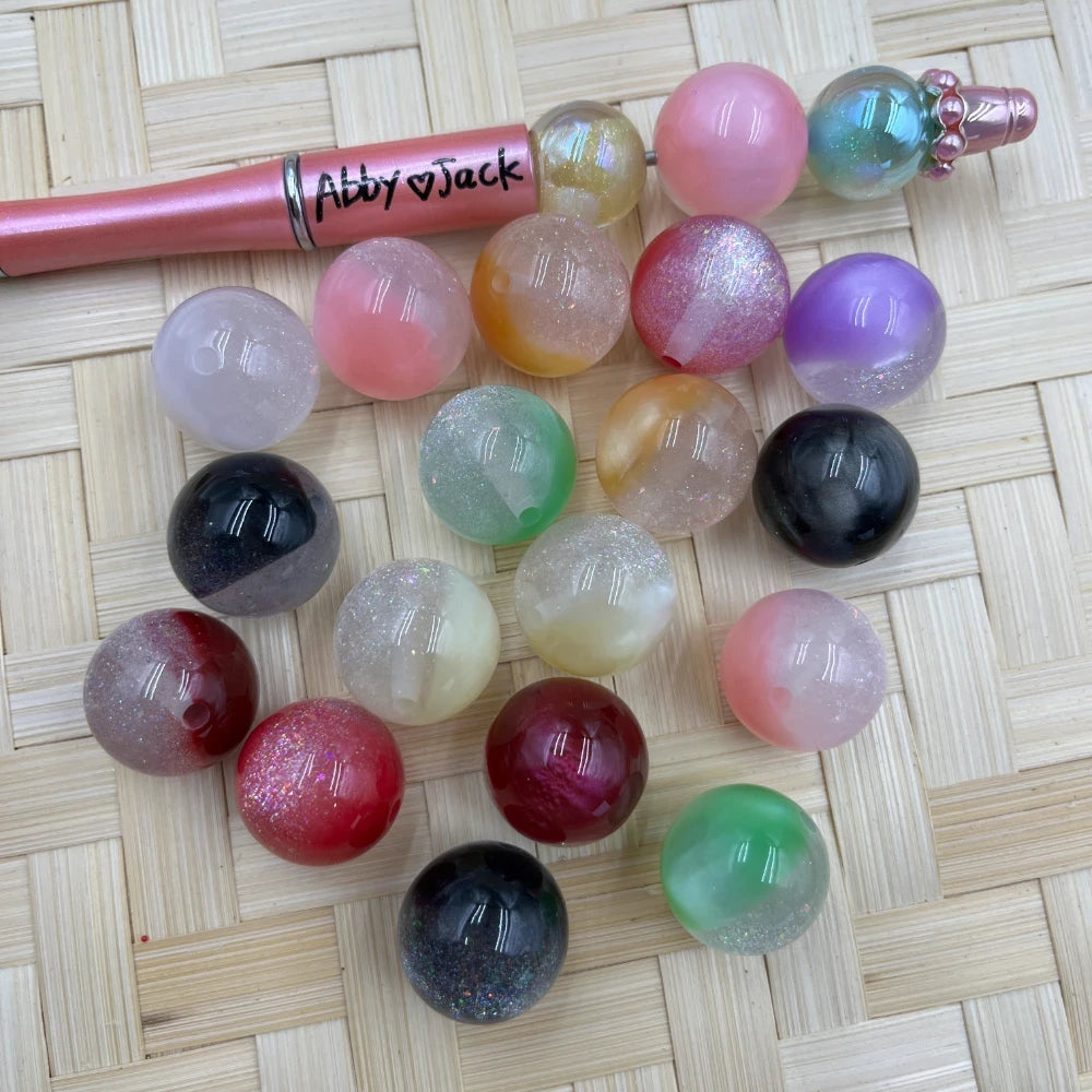 20MM galaxy glitter cat eye acrylic beads in assorted colors including black, red, pink, green, purple, and clear glitter on a woven surface next to a beadable pen.