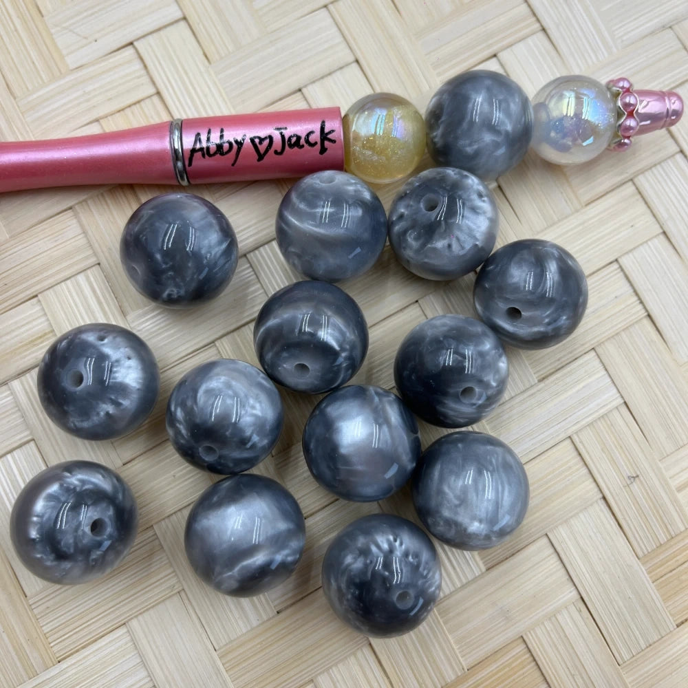 20MM gray marble swirl acrylic beads with pearlescent finish displayed on woven surface next to a beadable pen, showing drilled holes for DIY jewelry making.