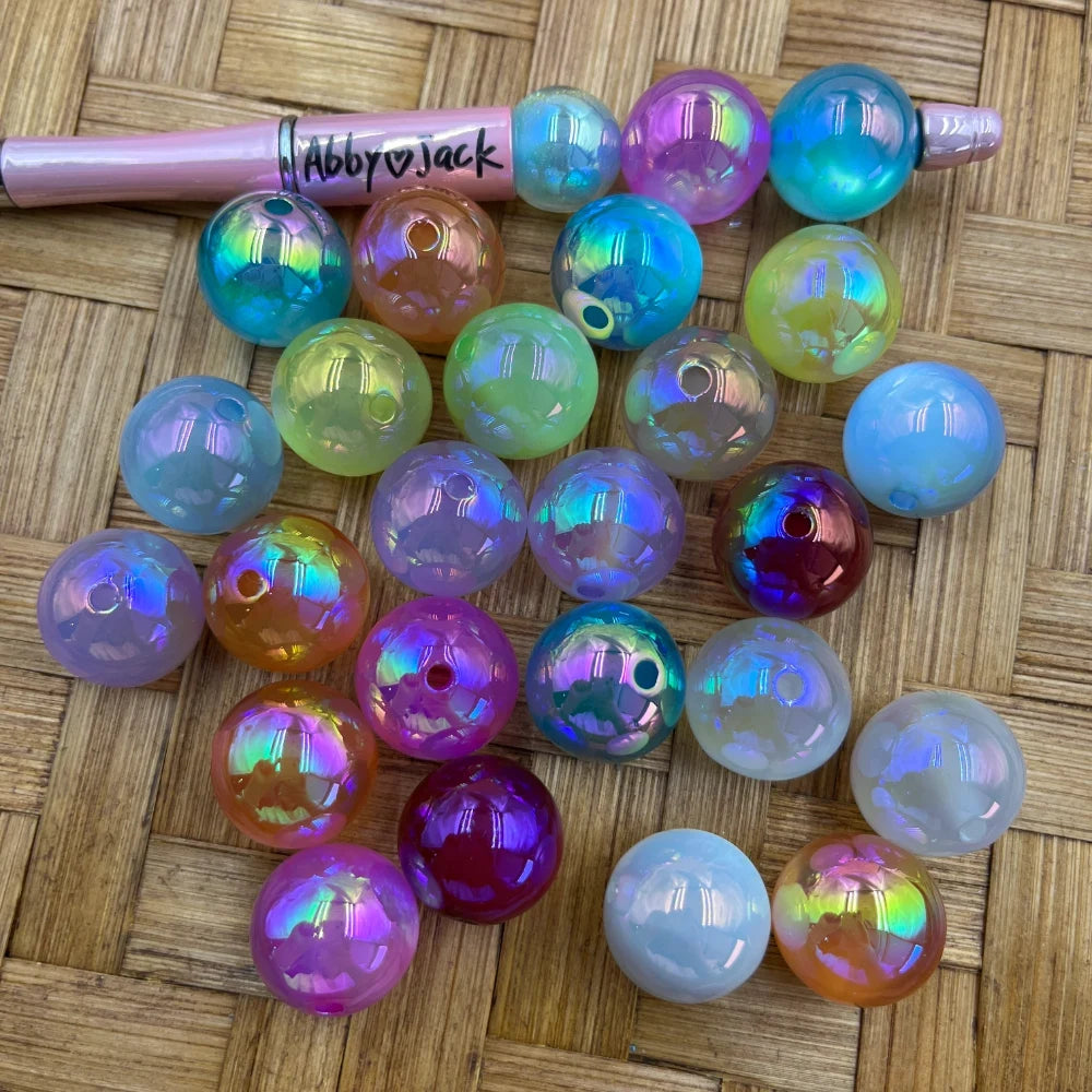 20MM iridescent AB finish bubblegum acrylic beads in assorted pastel and jewel tone colors including pink, purple, blue, green, orange and white with rainbow shimmer effect, shown on woven surface next to a pink beadable pen.