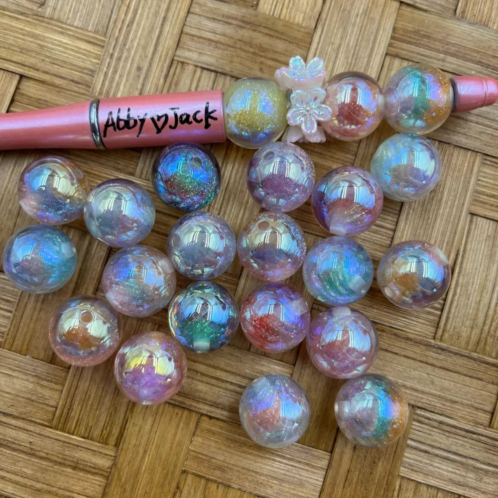 20MM iridescent galaxy glitter acrylic beads with aurora rainbow shimmer and colorful glitter inclusions displayed on wicker surface next to a beadable pen