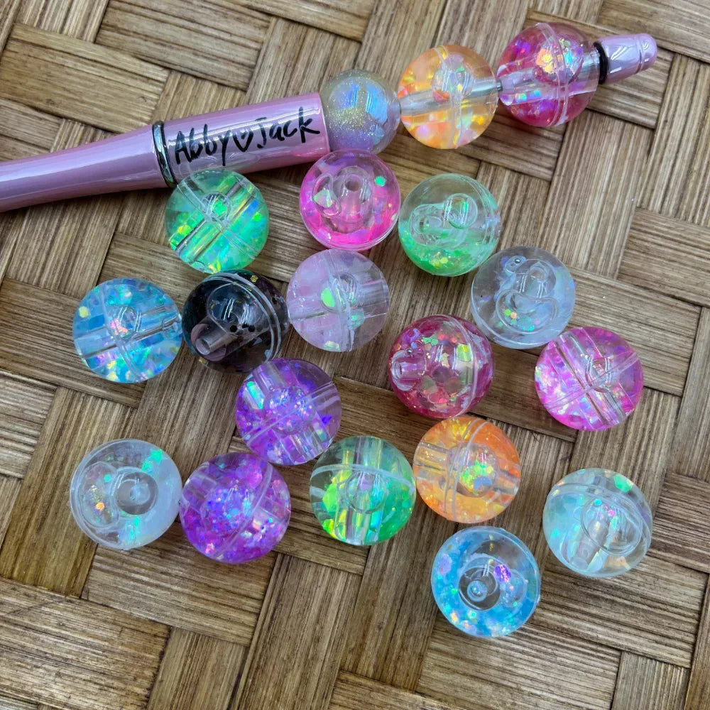 20MM iridescent glitter acrylic beads in assorted pastel and multicolor finishes displayed on a woven surface next to a pink beadable pen, showing holographic sparkle effect.