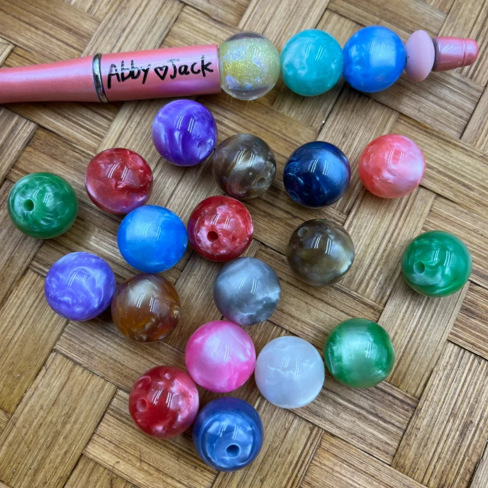 20MM marbled swirl acrylic beads in assorted colors including purple, blue, green, red, pink, gray, and brown on a woven surface next to a beadable pen labeled Abby and Jack.