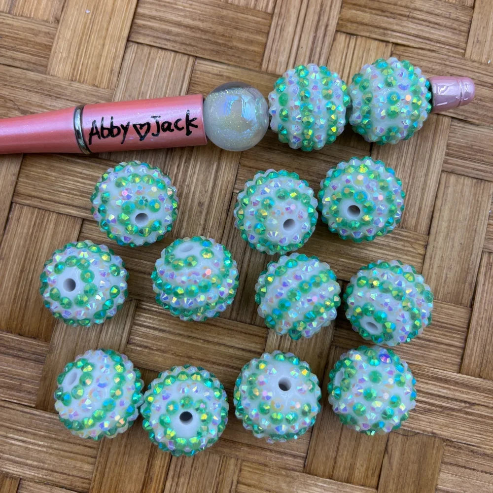 20MM mint green aurora borealis rhinestone beads with white base and iridescent green crystal embellishments, shown next to a beadable pen on a wicker surface.