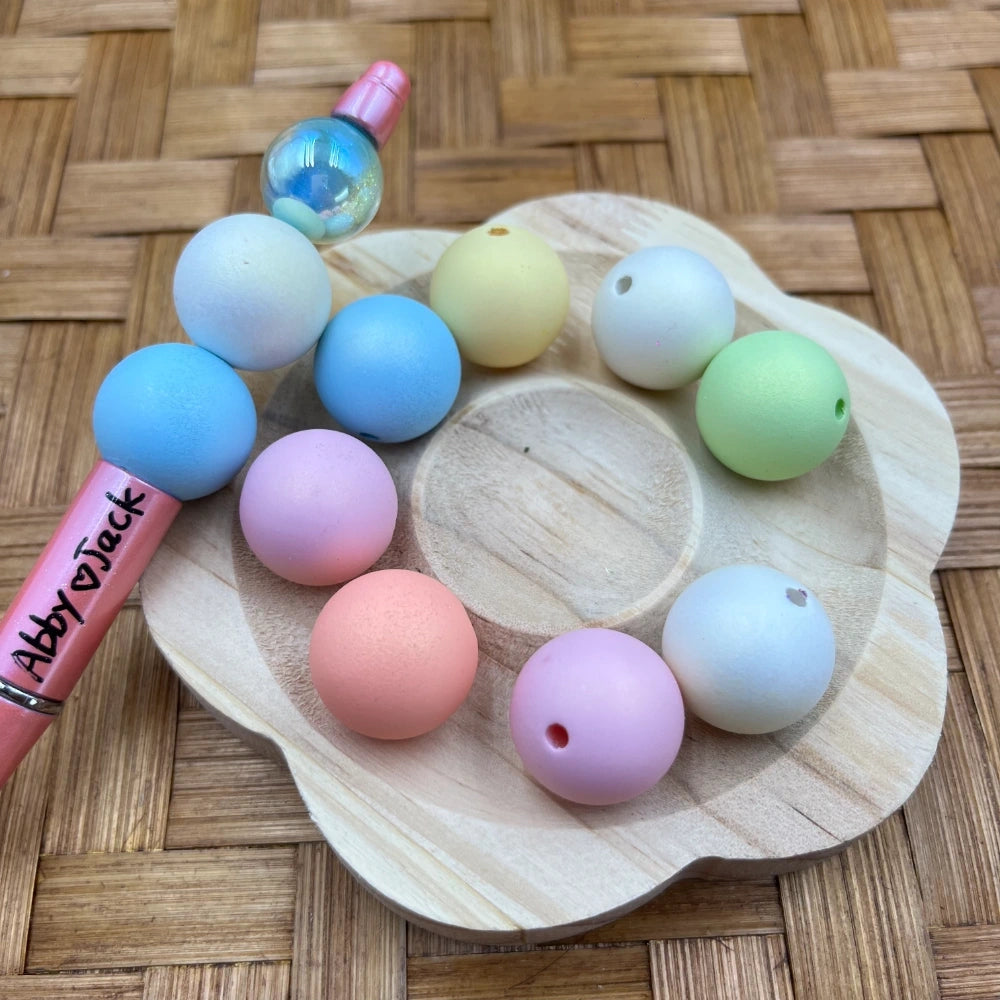 20MM pastel rainbow matte acrylic beads in soft pink, blue, lavender, peach, yellow, and green displayed on a wooden tray with a beadable pen for scale.