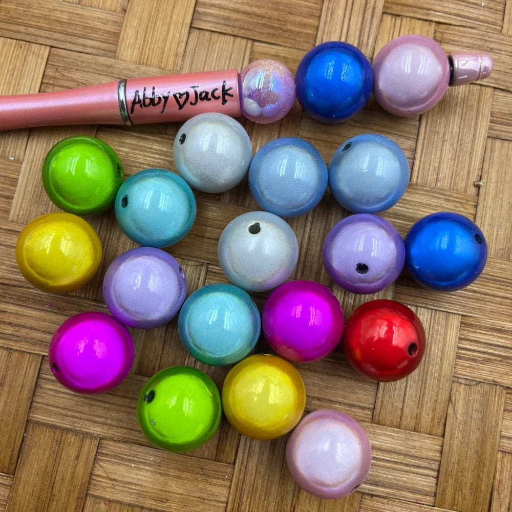 Assorted 20mm pearlescent shimmer acrylic beads in rainbow colors including pink, blue, green, yellow, purple, teal, magenta, red and white displayed on a woven surface next to a beadable pen.