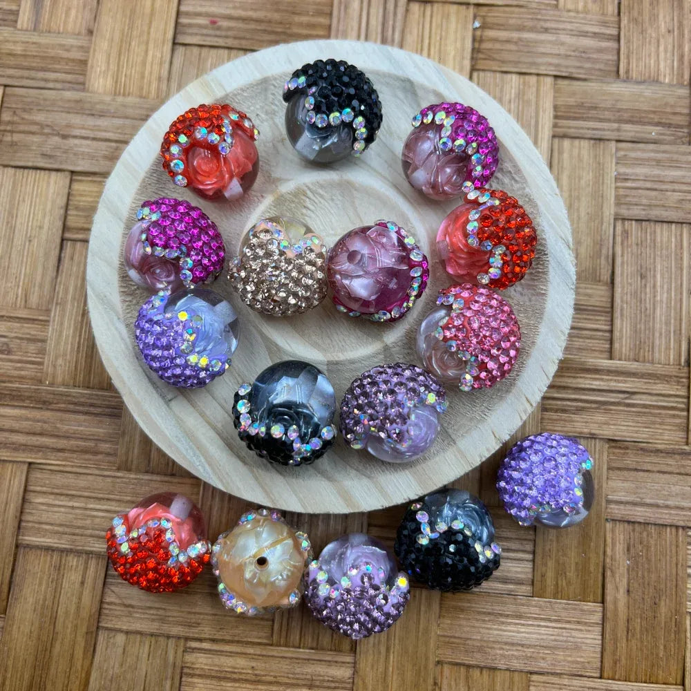 Assorted rhinestone half pave and rose carved resin fancy beads in pink, purple, black, red, and champagne colors displayed on a round wooden tray