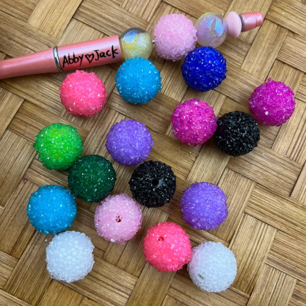 20MM multicolor rhinestone sugar beads in pink, blue, green, purple, black, white, and hot pink displayed on woven surface next to a beadable pen labeled Abby heart Jack
