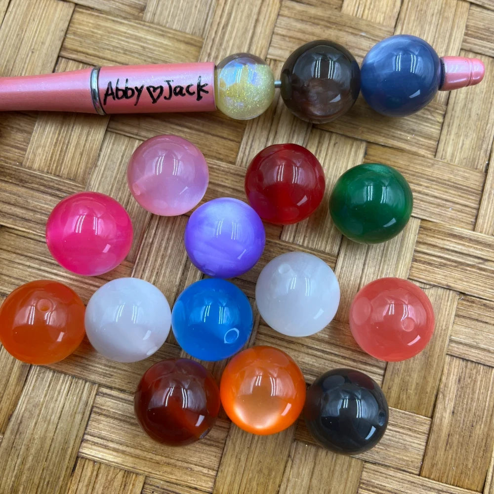 20MM solid color acrylic beads in assorted colors including pink, red, green, blue, purple, white, orange, black, and brown displayed on a woven surface next to a beadable pen.