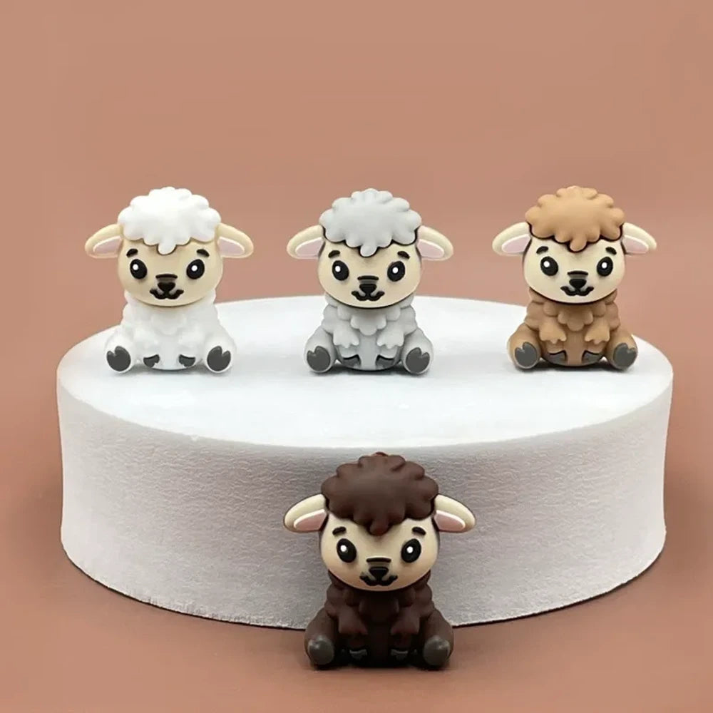 Four cute 3D silicone focal beads shaped like sitting lambs in white, gray, tan, and dark brown colors displayed on a white pedestal against a pink background.