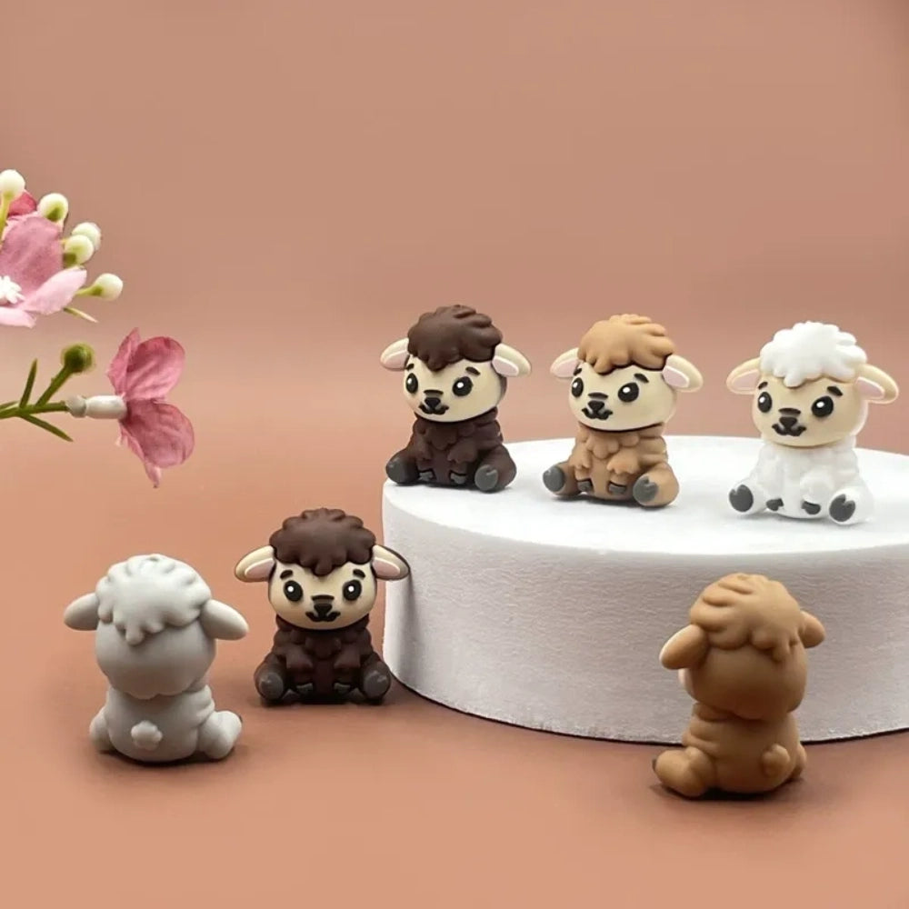 Six miniature 3D silicone focal beads shaped like cute sitting lambs in brown, tan, grey, and white colorways displayed on a white platform with pink flowers on a mauve background. - Random Mixed