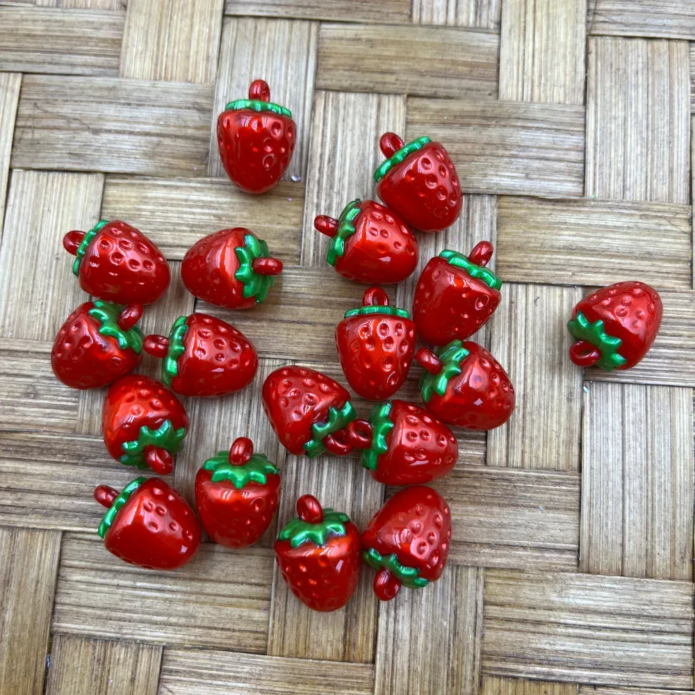 Shiny red and green 3D strawberry-shaped resin bail beads scattered on a woven bamboo surface, perfect for beadable pens, keychains, and DIY jewelry making.