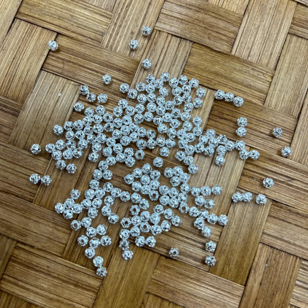 6MM silver filigree ball metal spacer beads scattered on a woven bamboo surface, showing textured hollow round design for DIY jewelry making and beadable pens.