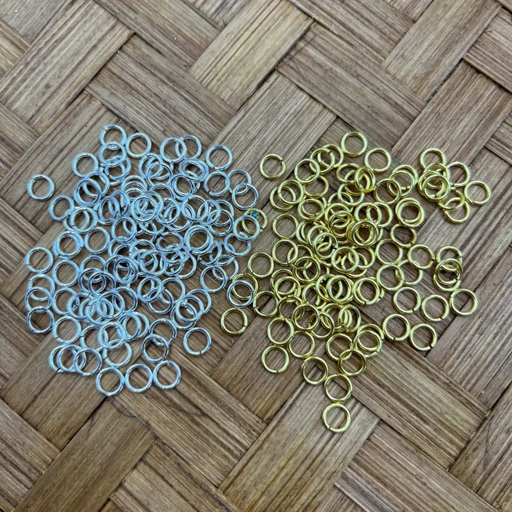 6MM silver and gold metal jump rings spread on a woven bamboo surface, used for DIY jewelry making, keychains, beadable pens, and bracelets.