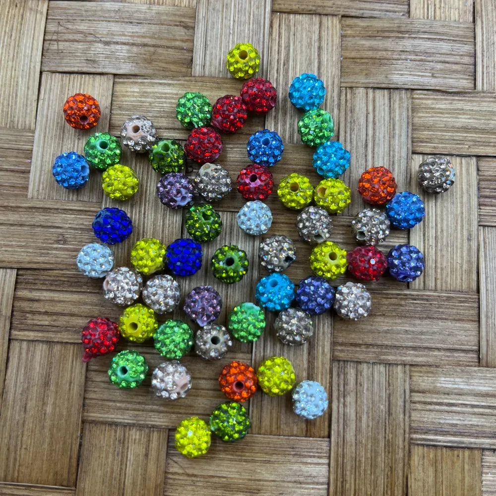 8MM mixed color clay rhinestone beads in assorted colors including red, blue, green, yellow, purple, orange, clear, and teal displayed on a woven bamboo surface for DIY jewelry making and beadable pens.