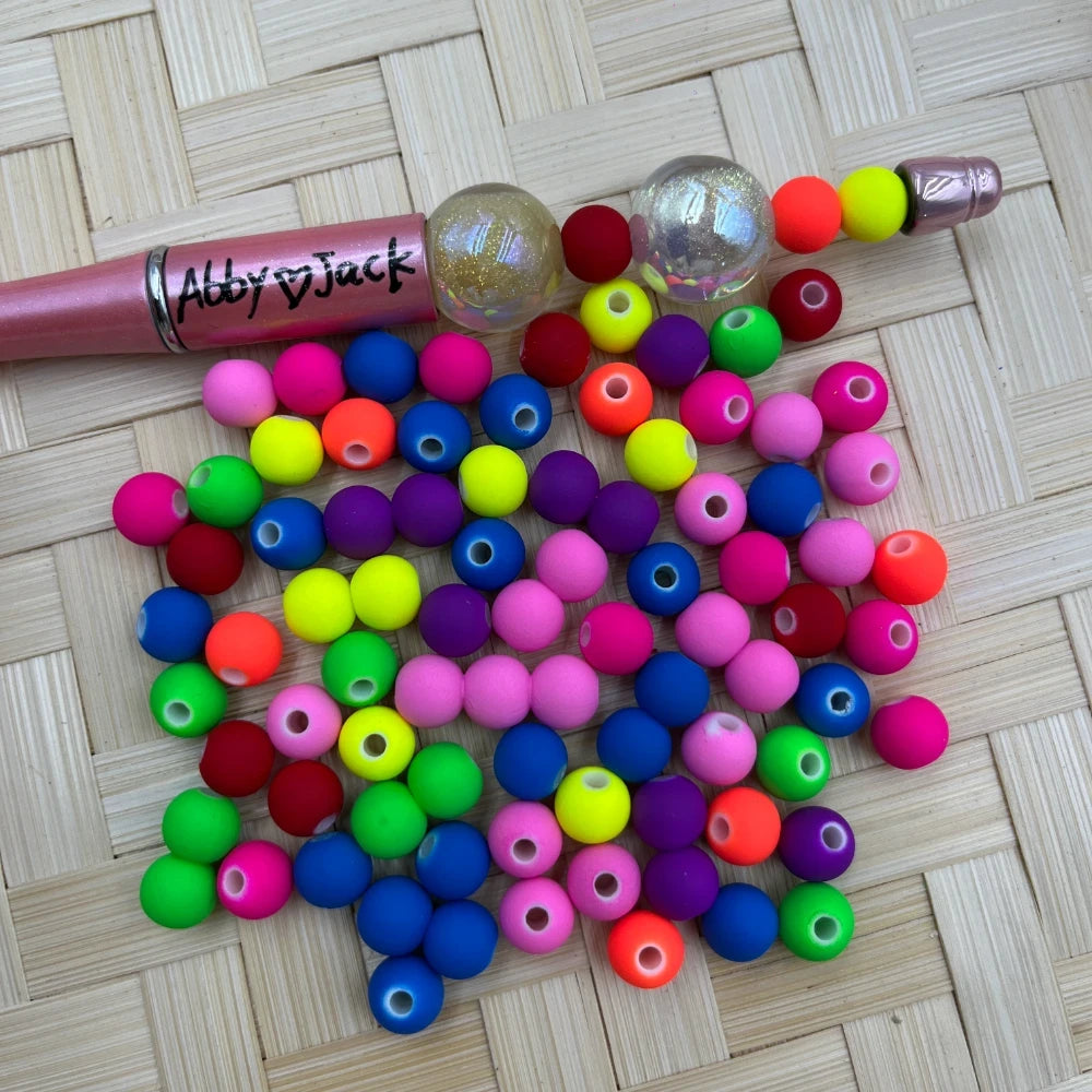8MM neon matte rubber finish acrylic beads in mixed colors including pink, blue, yellow, green, orange, red and purple, displayed with a beadable pen on a wicker surface.