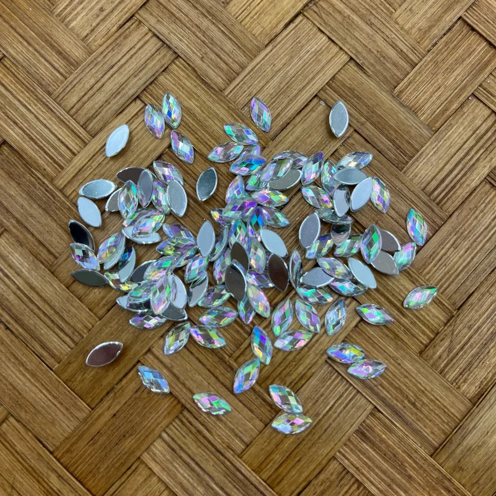 Iridescent AB crystal marquise eye-shaped flatback rhinestone fancy beads scattered on woven bamboo surface, showing rainbow multi-color sparkle and silver flat backs.
