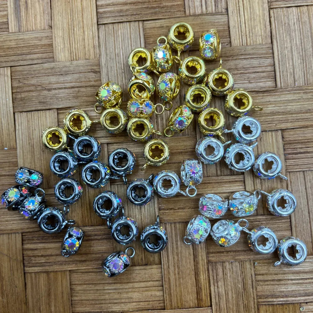 Assorted AB crystal rhinestone bail beads in gold, gunmetal black, and silver finishes with iridescent sparkle stones and large-hole barrel design, arranged on woven bamboo surface.