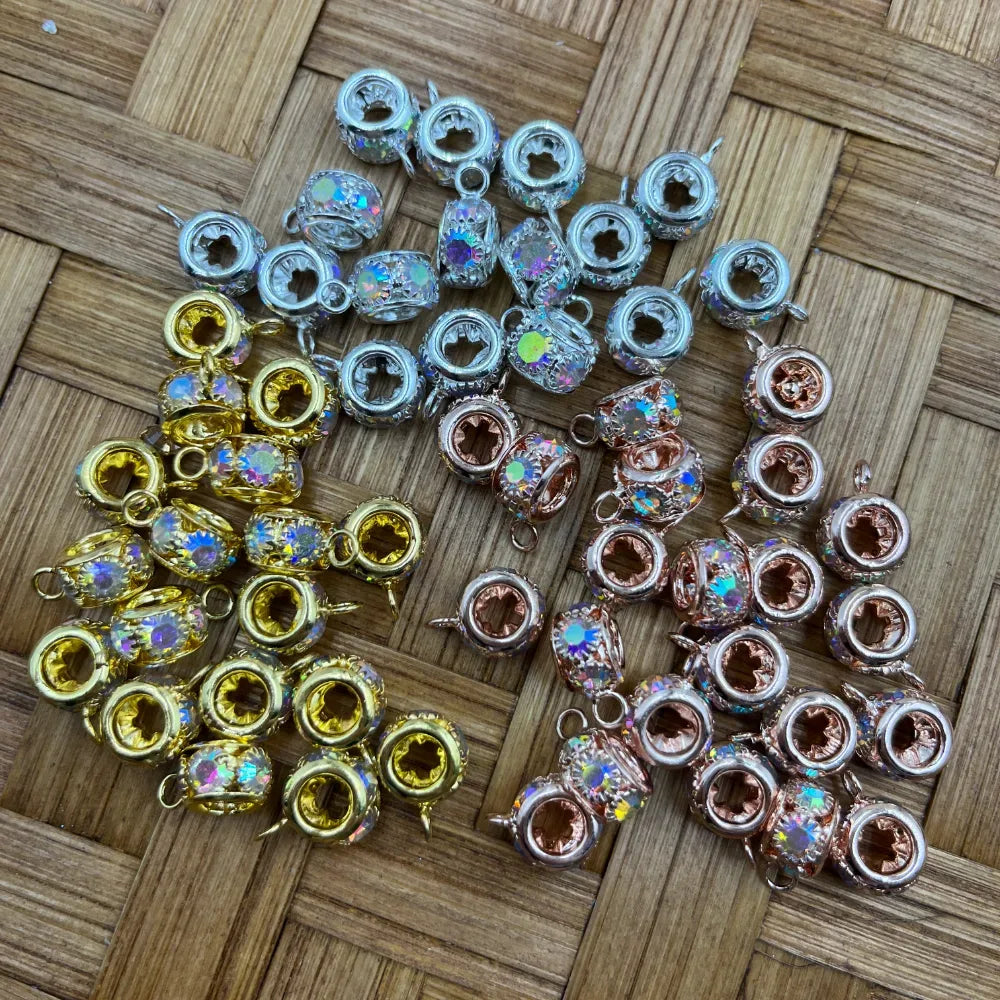 AB crystal rhinestone bail beads in gold, silver, and rose gold finishes arranged on a woven surface, featuring iridescent aurora borealis crystal centers with decorative metal settings and loop rings for DIY jewelry making.