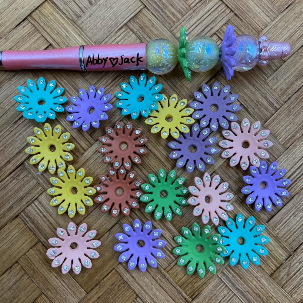 Assorted daisy rhinestone acrylic spacer beads in pastel and bright colors beside a pink decorated beadable pen