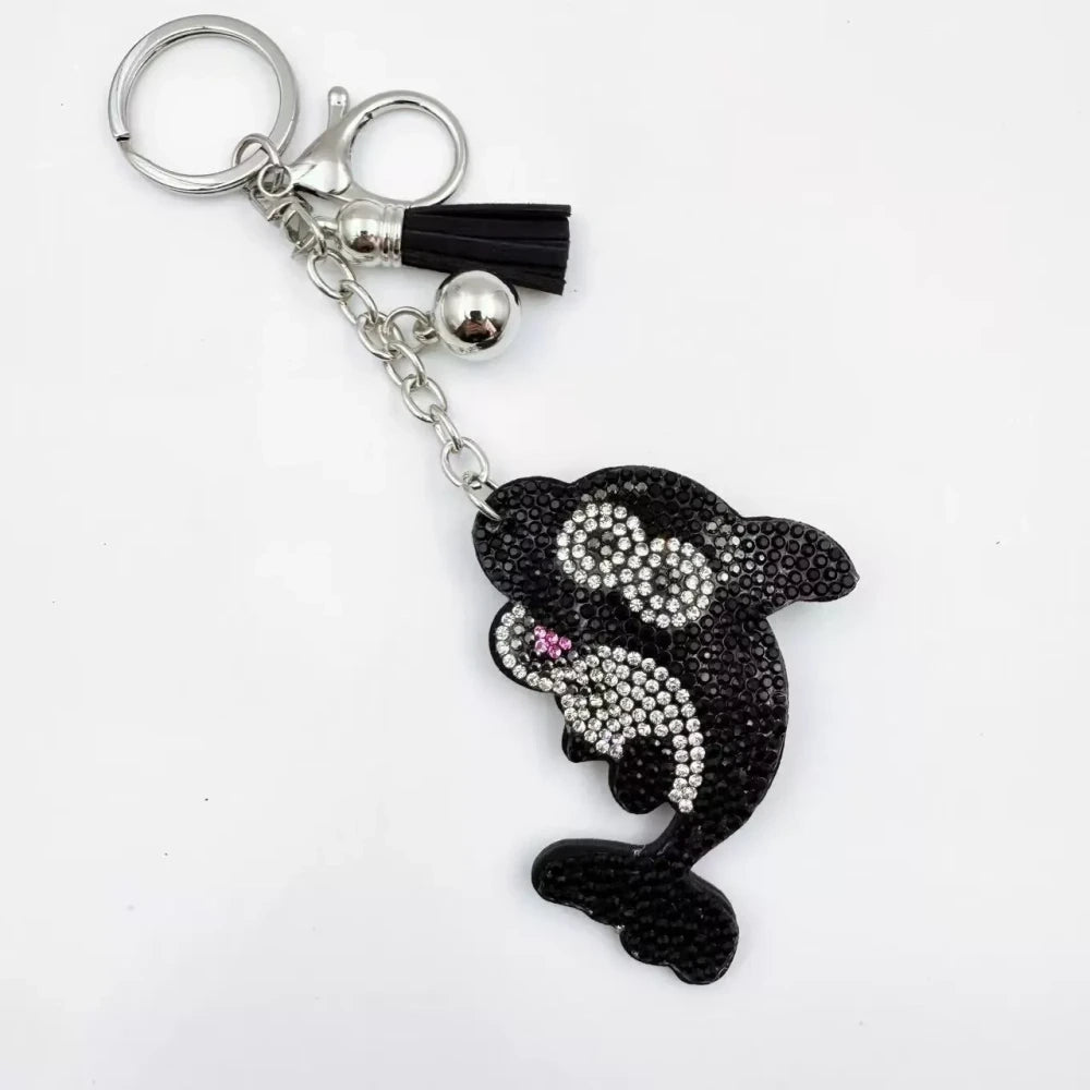 Four rhinestone dolphin charms in pink, aqua, black, and red with silver-tone rings, bells, and tassels on a white background. - Black