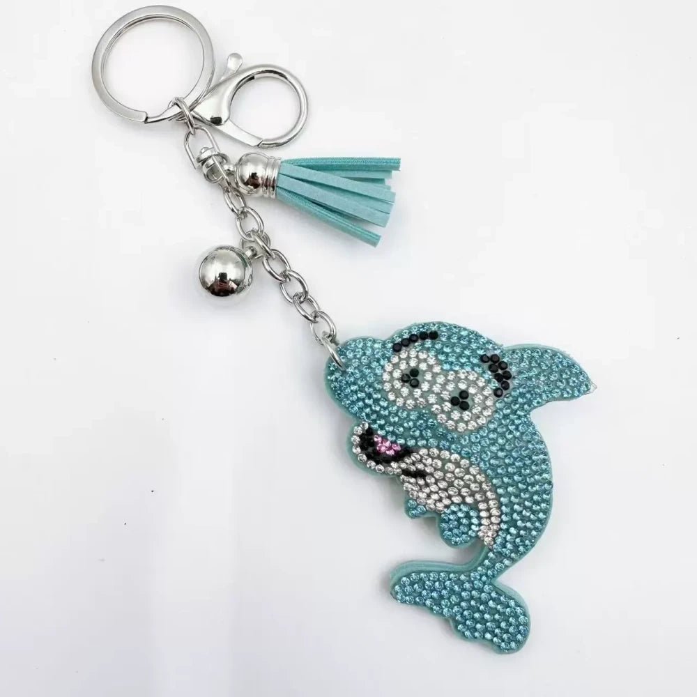 Four rhinestone dolphin charms in pink, aqua, black, and red with silver-tone rings, bells, and tassels on a white background. - Blue