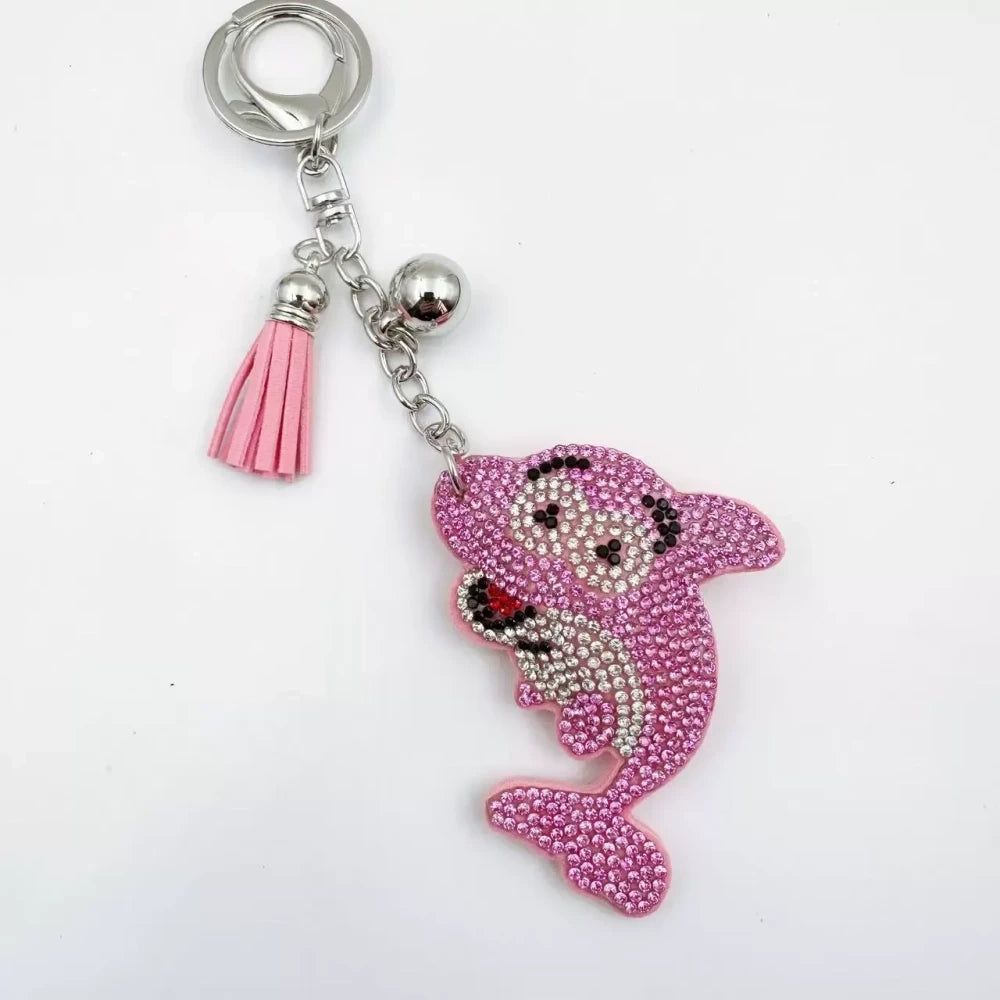 Four rhinestone dolphin charms in pink, aqua, black, and red with silver-tone rings, bells, and tassels on a white background. - Pink