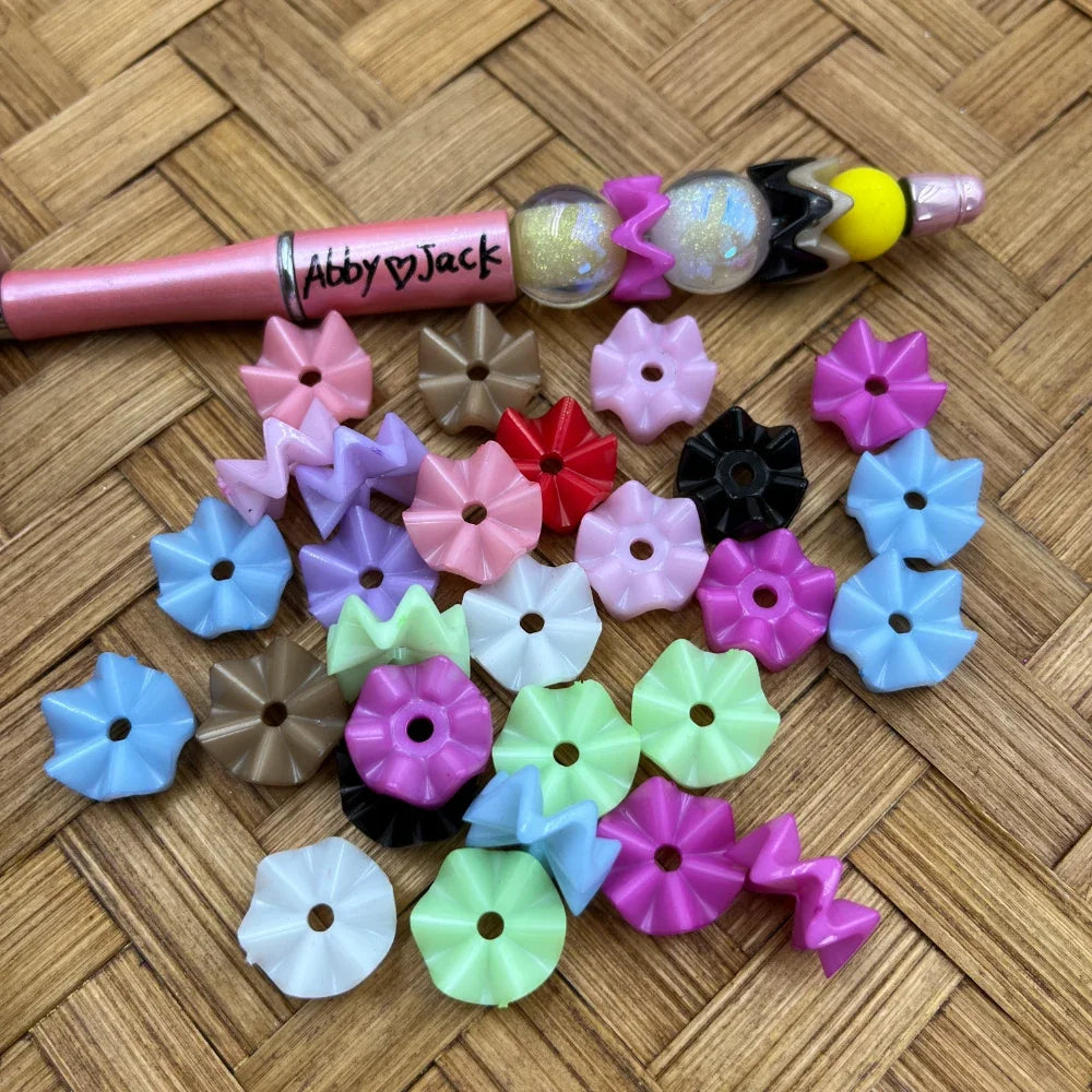 Assorted pastel flower and zigzag acrylic spacer beads with a beadable pen example on a woven wood background