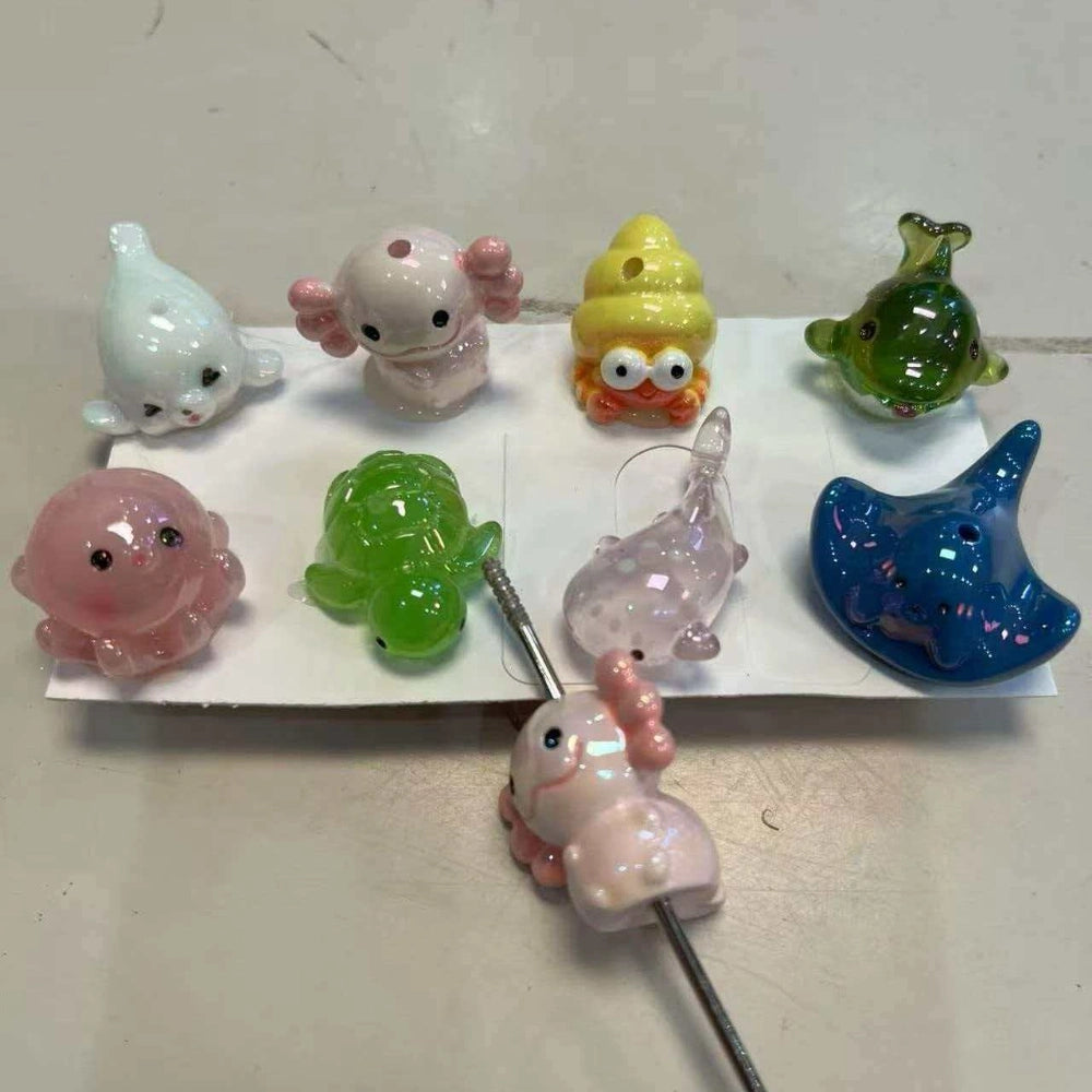 Assorted lampwork glass ocean animal straw toppers including axolotl, turtle, octopus, ray, seal, crab, and fish in pastel colors.