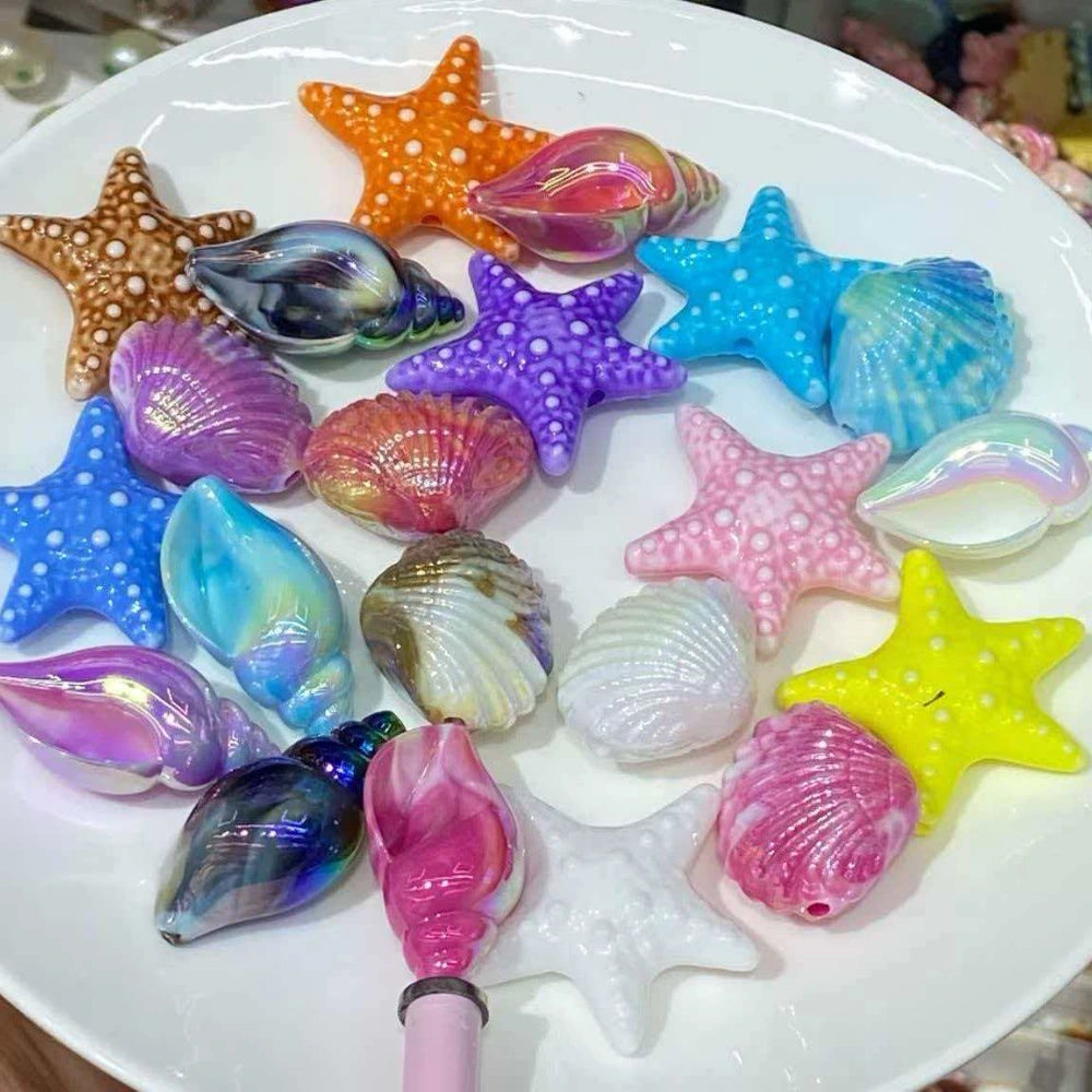 Assorted glossy iridescent resin shell and starfish straw toppers in pastel blue, pink, purple, yellow, orange, and white on a white plate