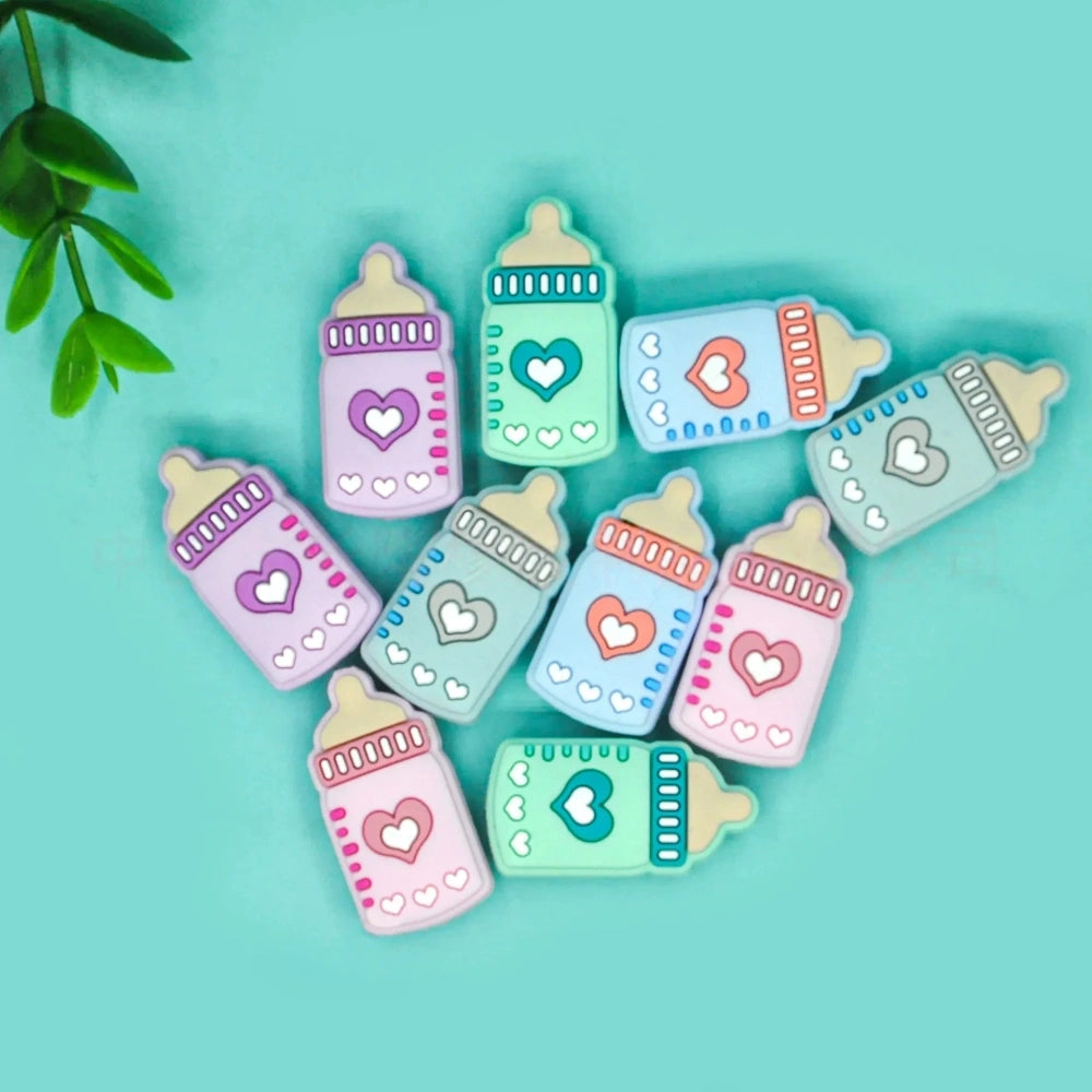 Assorted pastel silicone baby bottle flatback focal beads with heart designs in purple, teal, blue, gray, and pink on a mint background.
