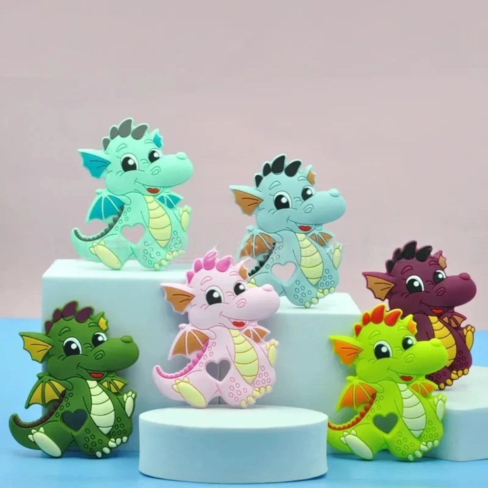 Six colorful baby dragon silicone focal beads in mint, blue, pink, green, lime, and purple displayed on white risers, featuring heart cutout belly and wing details for DIY craft projects.