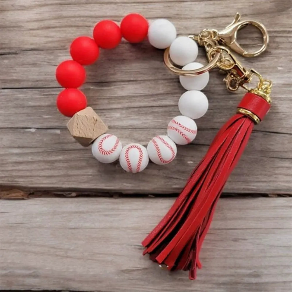 Baseball print silicone beads in red and white shown on beaded wristlet keychains with red leather tassels and gold hardware on a rustic wood background. - 2