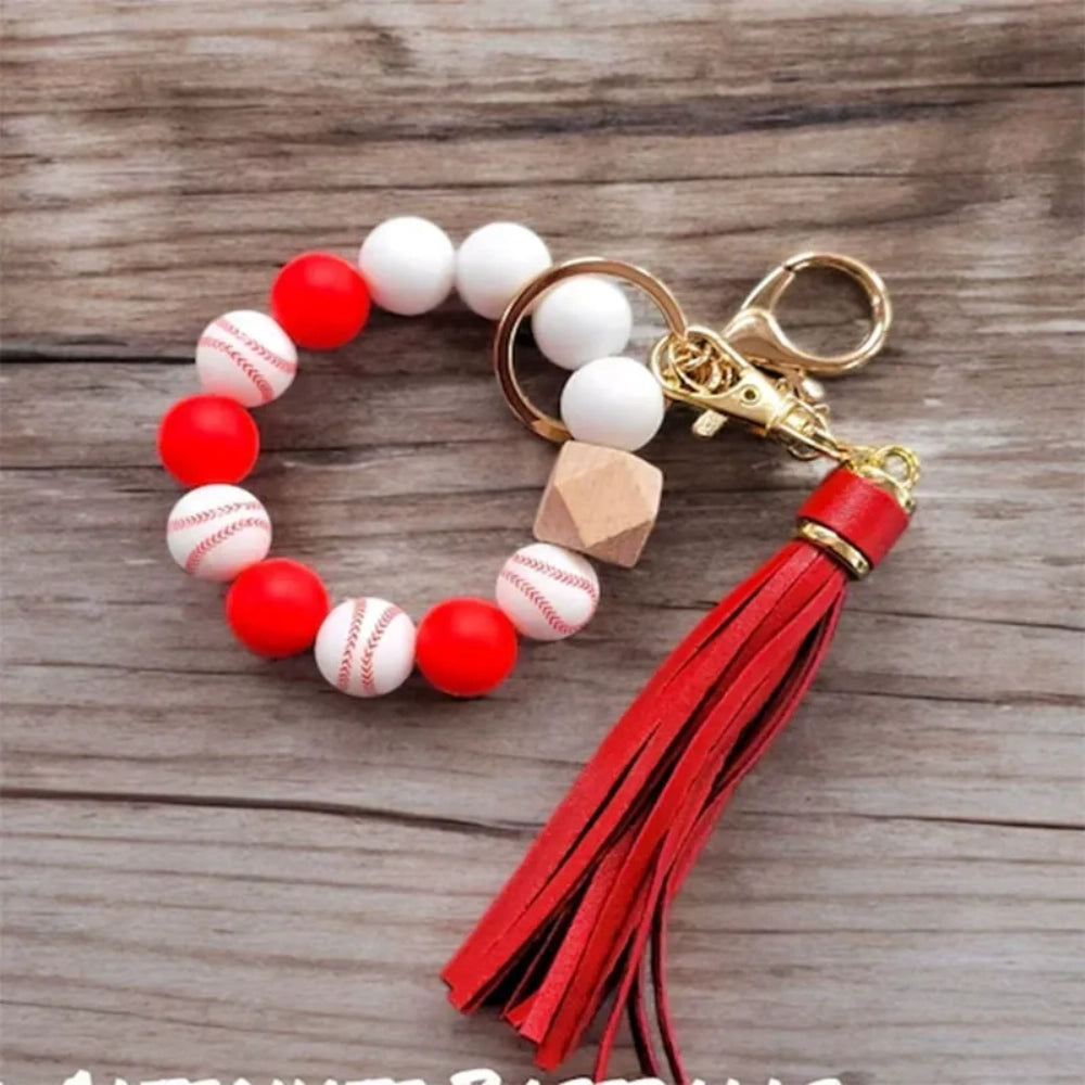 Baseball print silicone beads in red and white shown on beaded wristlet keychains with red leather tassels and gold hardware on a rustic wood background. - 4