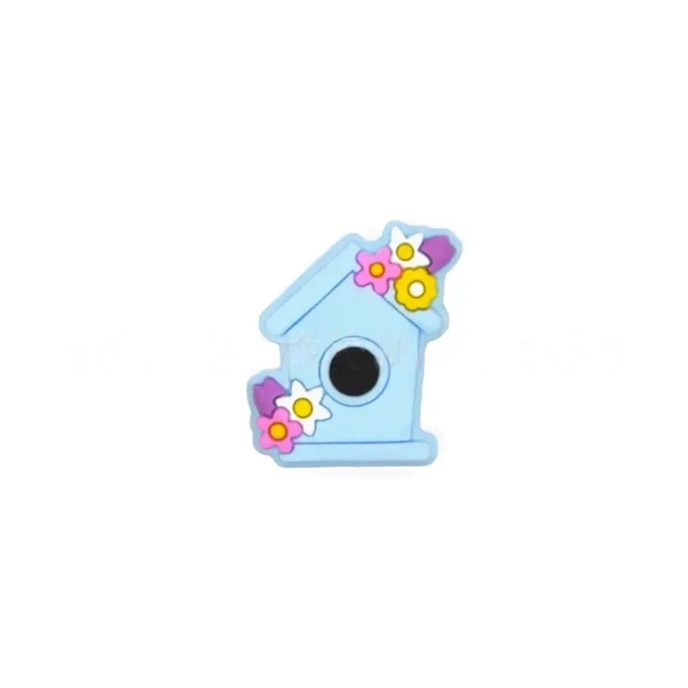 Six pastel silicone focal beads shaped like birdhouses decorated with flowers in pink, lavender, yellow, teal, mint, and blue colors displayed on a miniature white bench. - Light Blue