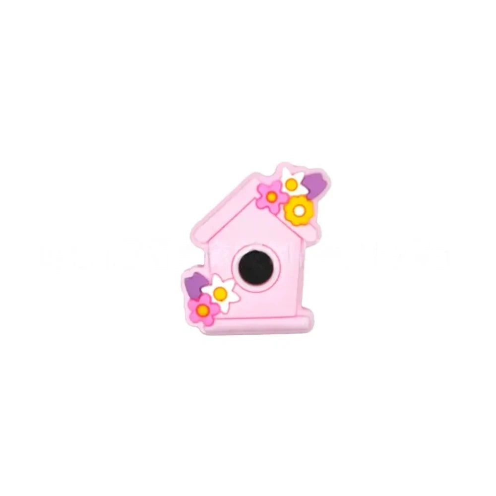 Six pastel silicone focal beads shaped like birdhouses decorated with flowers in pink, lavender, yellow, teal, mint, and blue colors displayed on a miniature white bench. - Light Pink