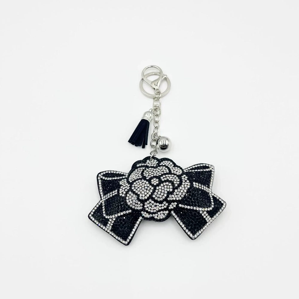 Black sequin and rhinestone rose bow keychain charm with silver tassel, bell, and lobster clasp on white background