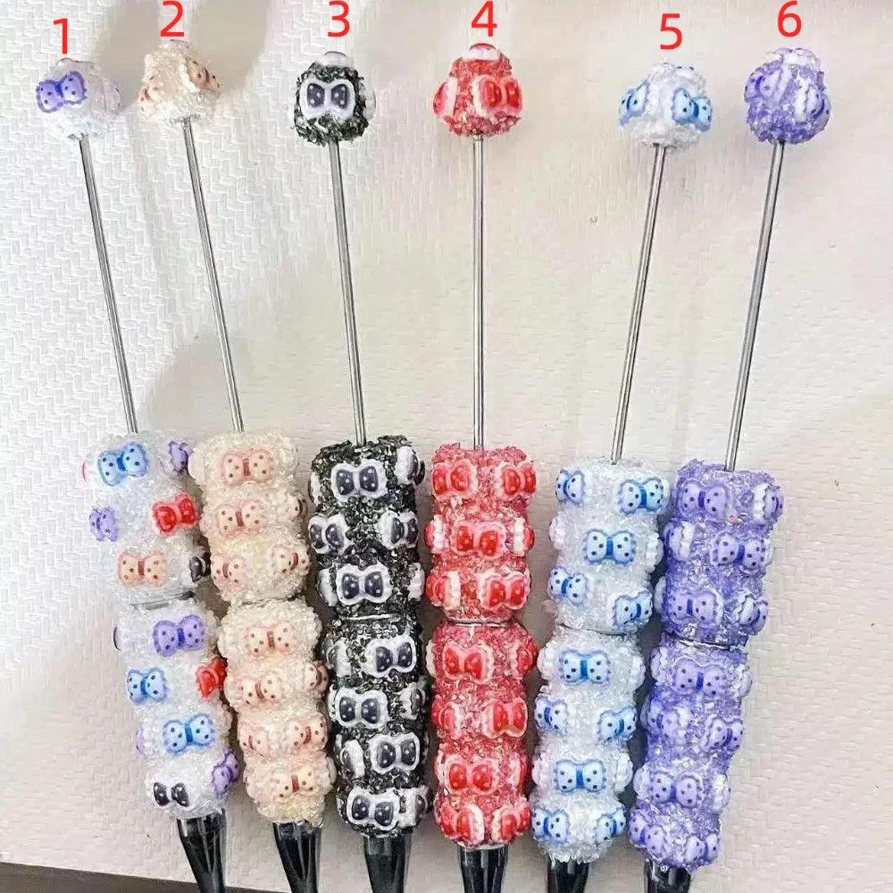 Set of 6 rhinestone beadable pens with bow tie pattern beads in white, black, red, pink, light blue, and purple glitter finishes, numbered 1 through 6.