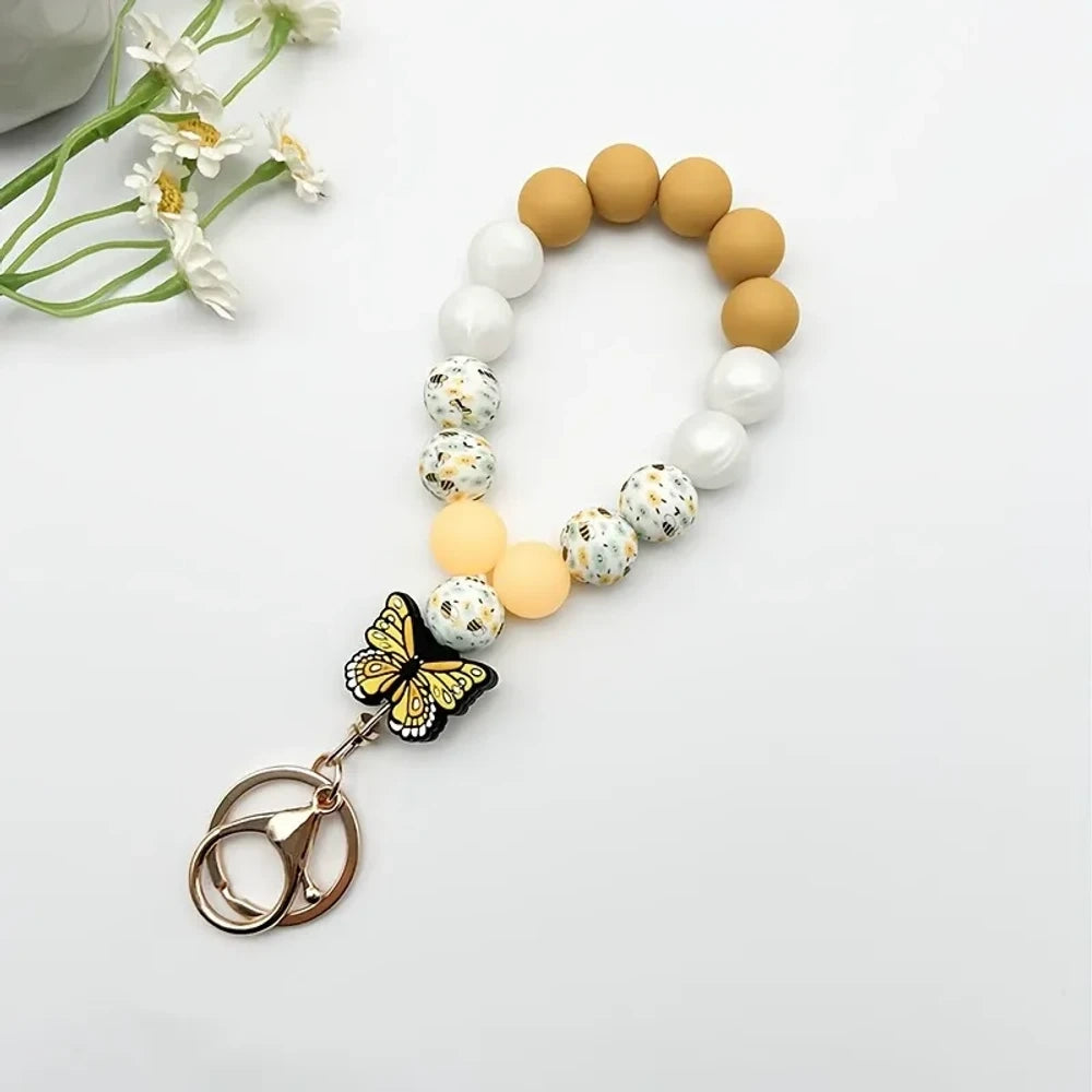 Assorted butterfly charm silicone bead bracelets arranged in a fan display featuring floral, leopard, rainbow, and solid color printed silicone beads with decorative butterfly pendants and daisy flowers at center. - Yellow