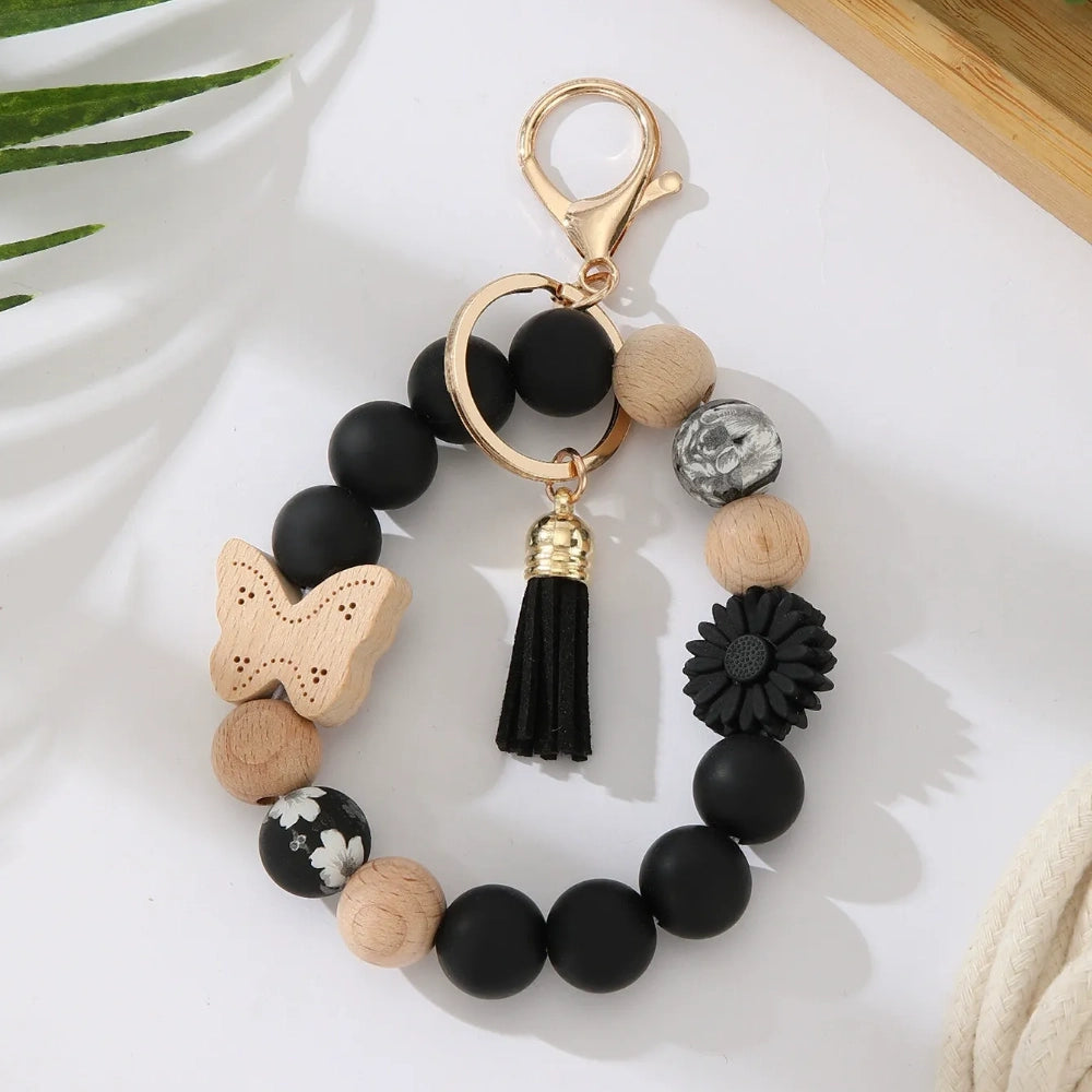 Assorted butterfly and flower silicone and wood bead keychain bracelets in pink, yellow, white, peach, black, purple, and green colorways with gold lobster clasp hardware and tassel accents for DIY jewelry making. - Black