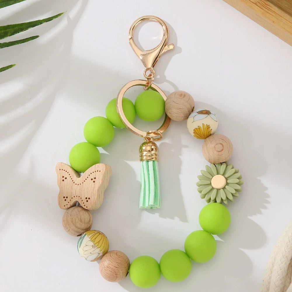 Assorted butterfly and flower silicone and wood bead keychain bracelets in pink, yellow, white, peach, black, purple, and green colorways with gold lobster clasp hardware and tassel accents for DIY jewelry making. - Green