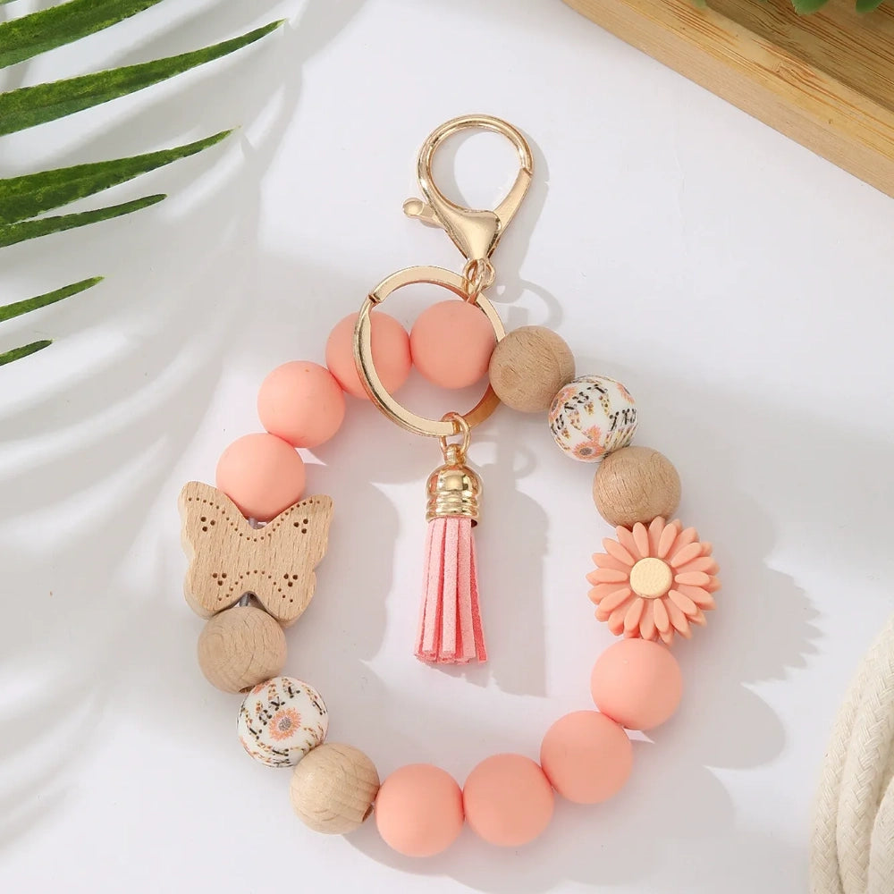 Assorted butterfly and flower silicone and wood bead keychain bracelets in pink, yellow, white, peach, black, purple, and green colorways with gold lobster clasp hardware and tassel accents for DIY jewelry making. - Orange